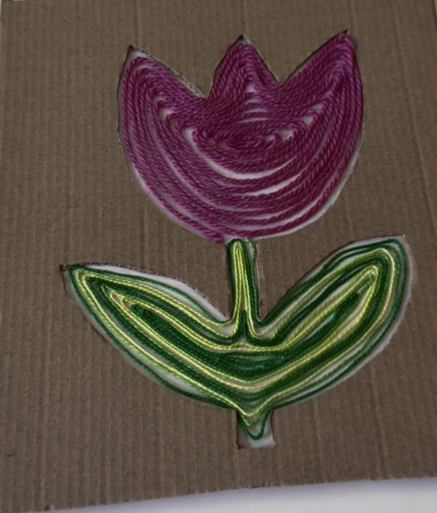 Purple yarn flower with green stem and leaves on cardboard