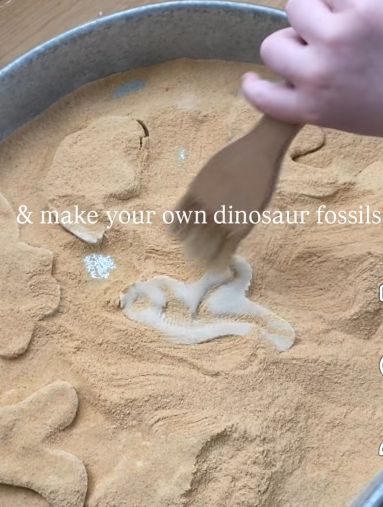 Child making a dinosaur fossil imprint in sand-colored dough